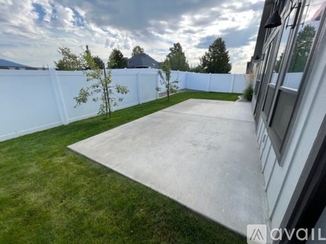 A backyard with a white fence and a concrete slab.