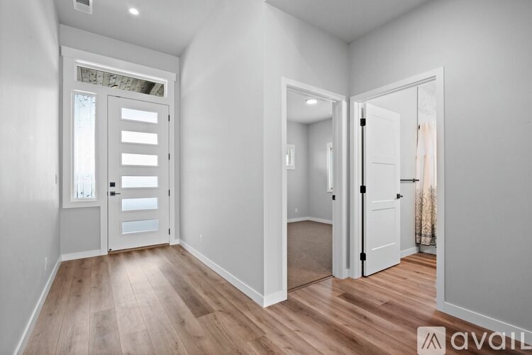 A room with wooden floors and white walls, with a door on the left and a mirror on the right.