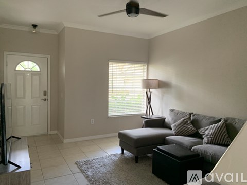 A living room with a grey couch, a black ottoman, and a floor lamp.