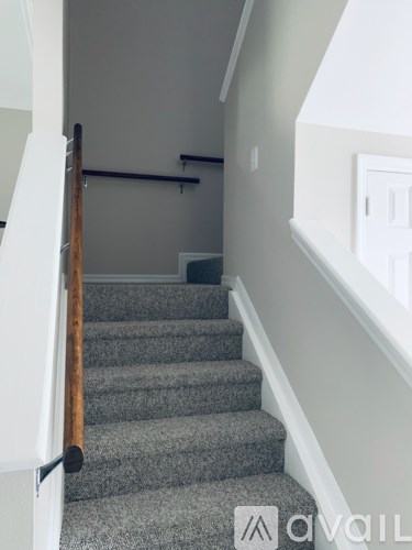 A staircase with a wooden handrail and grey carpeted steps.