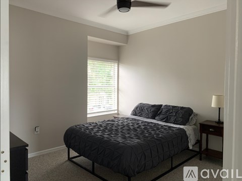 A bedroom with a bed, a nightstand, and a window with blinds.