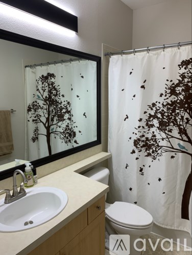 A bathroom with a white sink, toilet, and a shower curtain with a tree design.