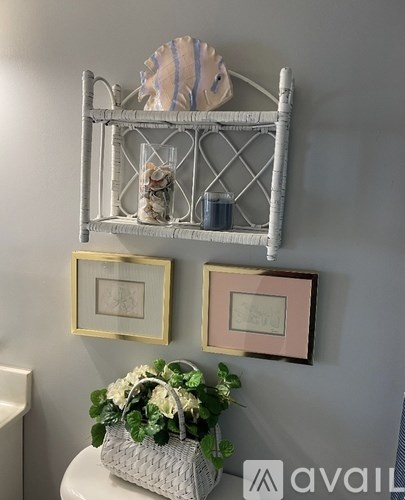 A white shelf with a basket of flowers and two picture frames on a wall.