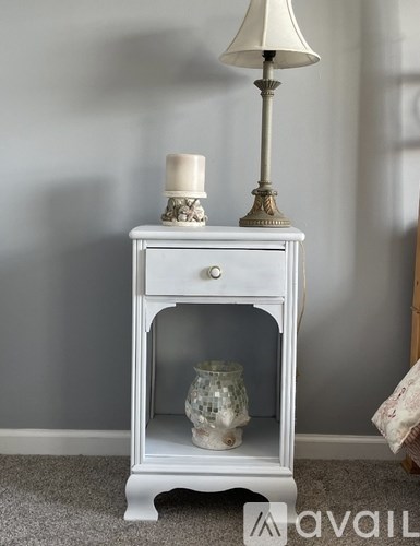 A white nightstand with a drawer and a shelf holding a vase.