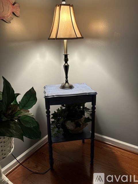 A lamp on a table with a plant behind it.
