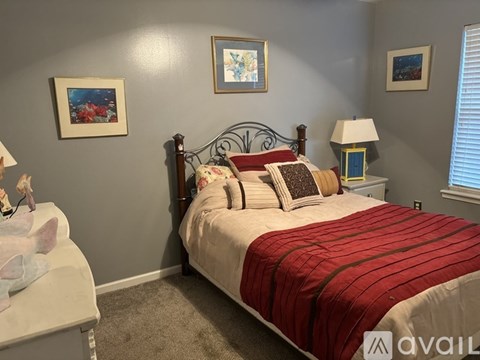A bedroom with a red bedspread and a white chair.