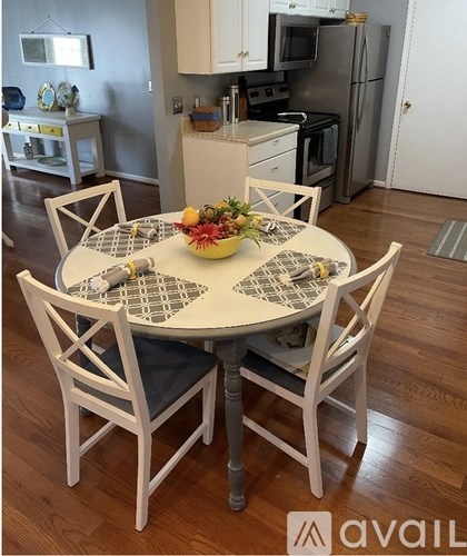 A white table with a bowl of fruit on it and chairs around it.