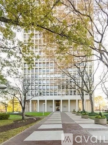 A modern building with a glass facade is surrounded by trees and a well-manicured lawn.