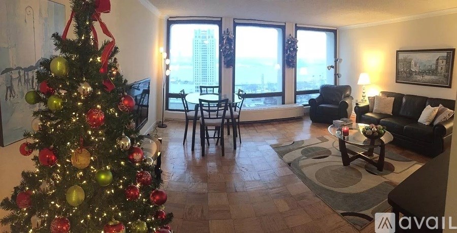 A Christmas tree with red and gold ornaments stands in a living room with a view of the city.