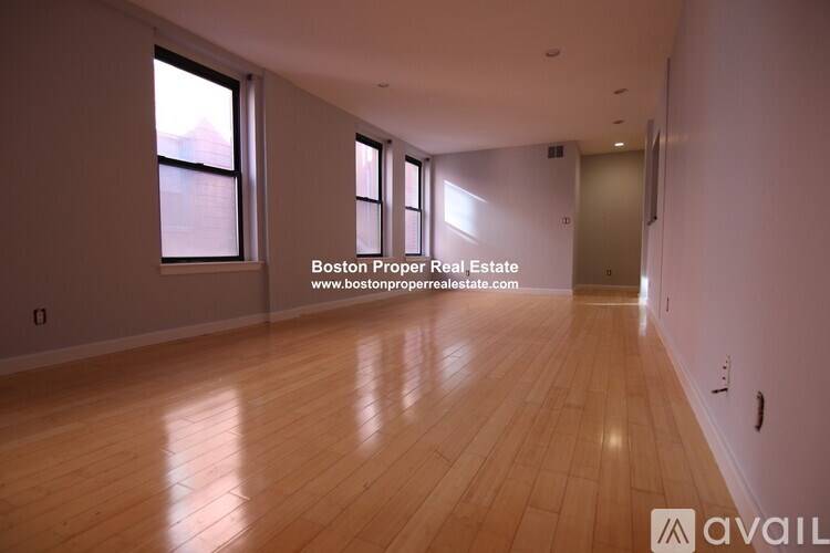 A spacious room with wooden flooring and large windows.
