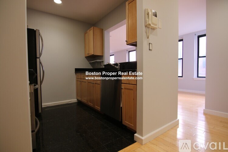 A kitchen area with a refrigerator, cabinets, and a phone on the wall.