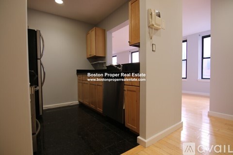 A kitchen area with a refrigerator, cabinets, and a phone on the wall.