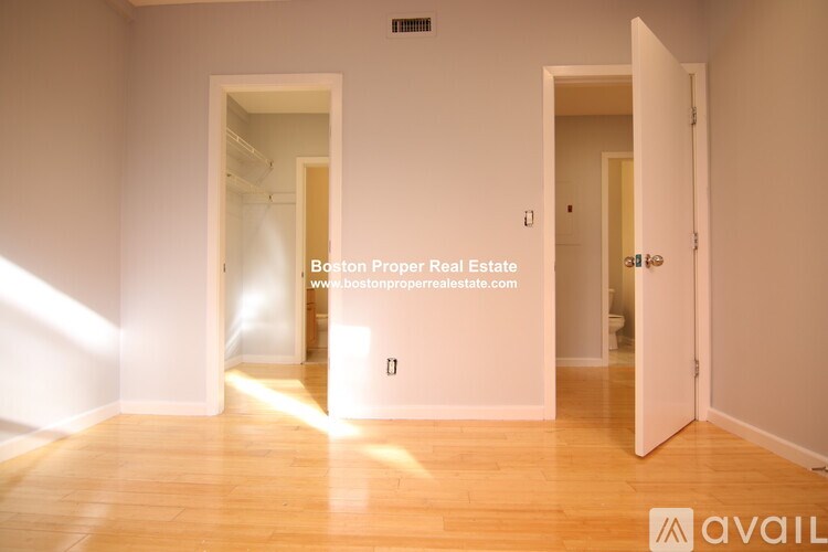 A room with wooden floors and white walls, with a doorway leading to another room.