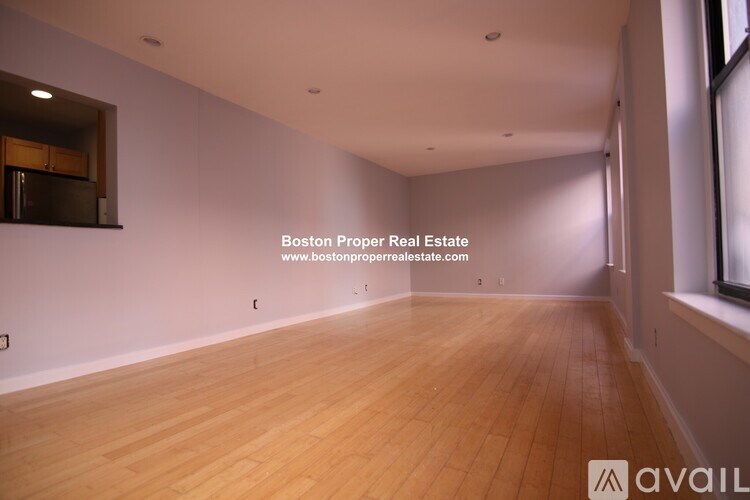 A large empty room with wooden floors and a window on the right side.