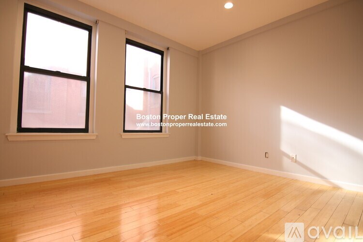 A room with wooden flooring and two windows is available for rent.