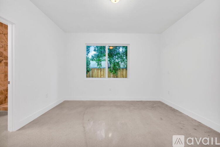 A room with a window showing a view of trees and a fence.
