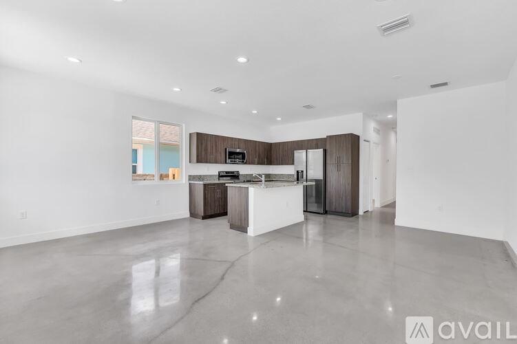 A spacious, empty room with a kitchen area in the background.