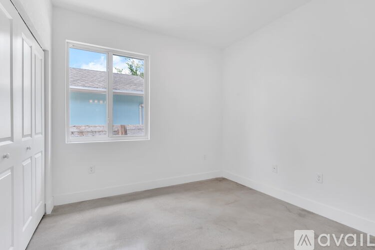 A room with a window showing a view of a house and trees outside.