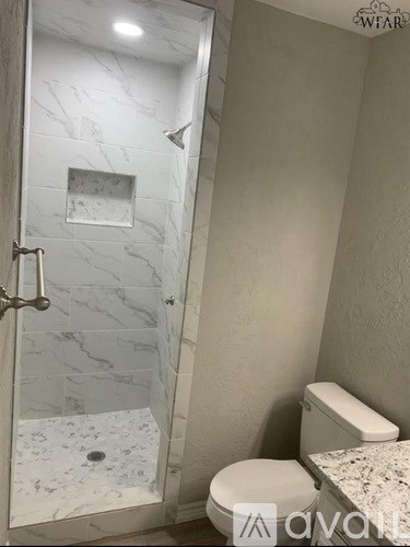 A white toilet sits next to a walk-in shower with a marble tile floor.