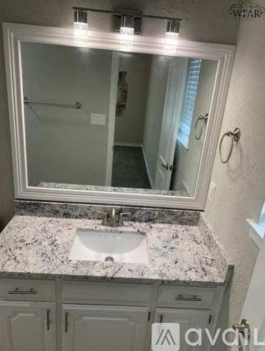 A bathroom with a granite countertop and a large mirror.