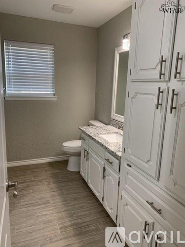 A bathroom with a toilet, sink, and cabinets.