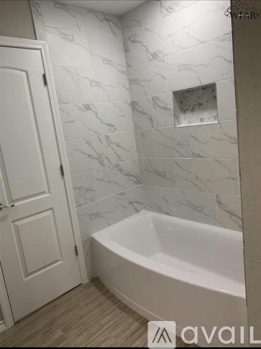 A white bathroom with a marble tile wall and a bathtub.