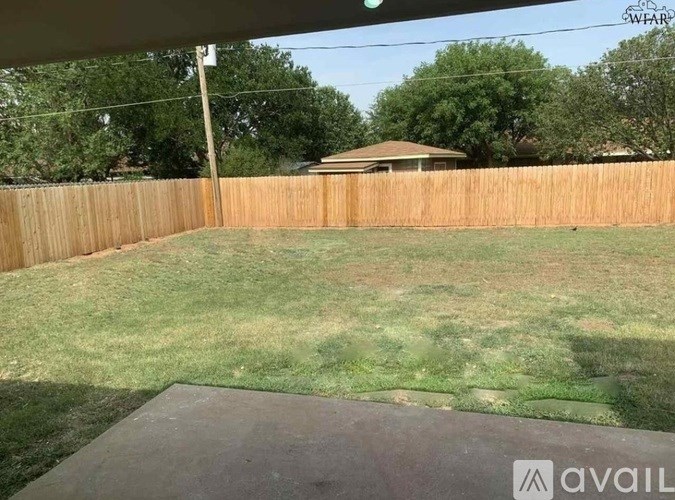 A backyard with a wooden fence and a covered patio area.