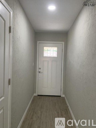A hallway with a white door and wooden floor.