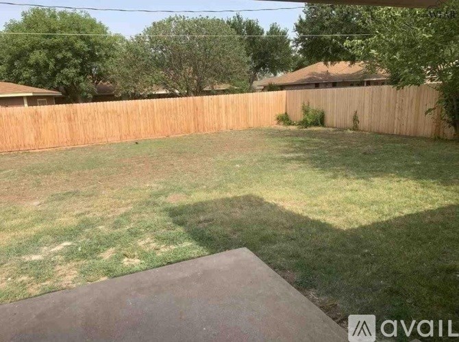 A backyard with a wooden fence and a concrete pathway.