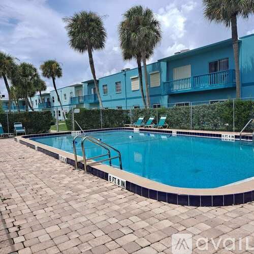 A swimming pool surrounded by palm trees and a blue building.