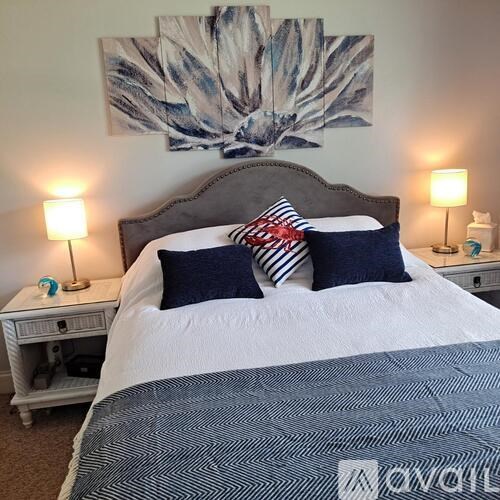 A bed with a white comforter and a grey headboard with a painting above it.