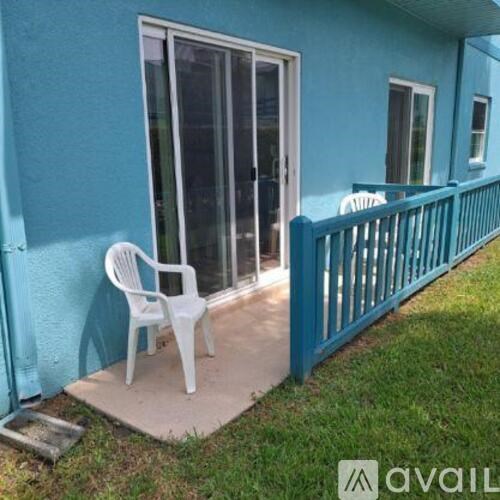 A white plastic chair is on a concrete slab outside a blue house.