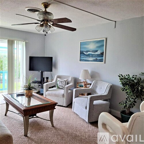 A living room with a ceiling fan, two chairs, a table, and a painting on the wall.