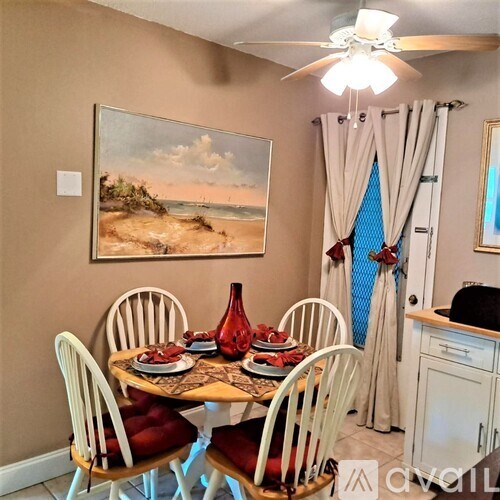 A dining room with a table set for four and a painting of a beach scene on the wall.