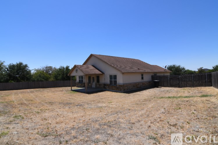 A house with a brown roof is surrounded by a fence and has a yard with dry grass.