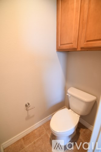 A white toilet in a small bathroom with wooden cabinets.