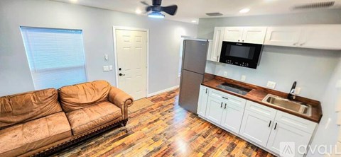 A living room with a couch and a kitchen area with a refrigerator and microwave.