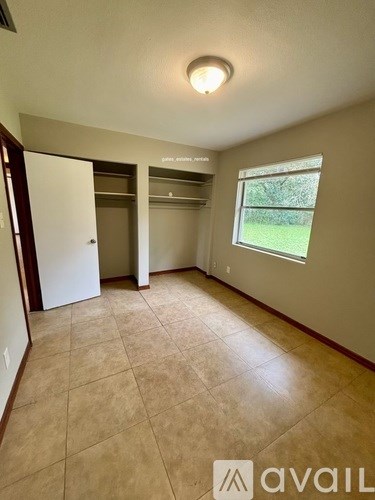 A room with beige tiled flooring and a window showing greenery outside.