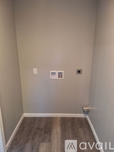 A room with a wooden floor and a white wall with a switch and a socket.