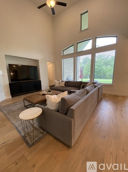 A living room with a grey couch, a television, and a ceiling fan.