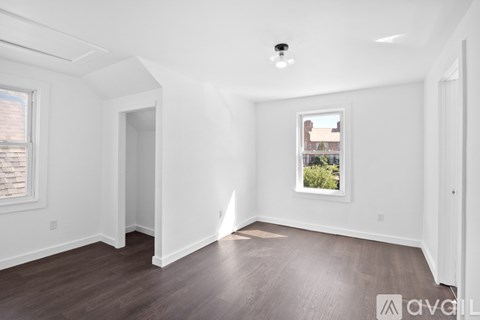 A room with wooden floors and white walls, a window with a view of a building outside, and a door on the right.