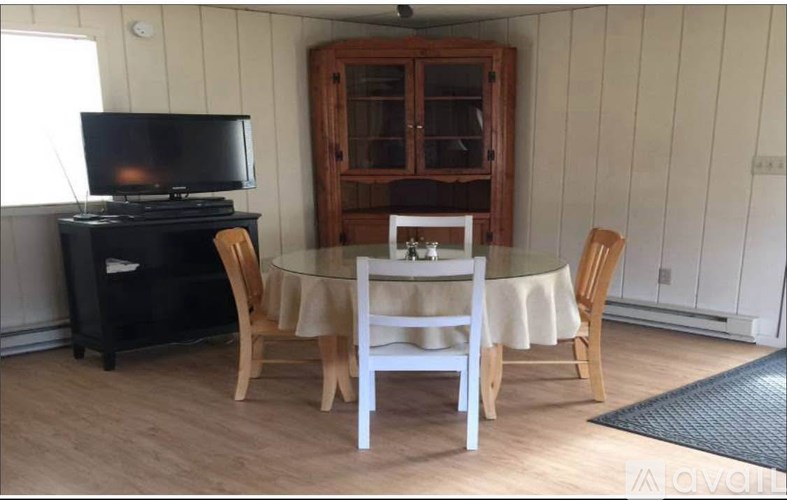 A black television sits on a black stand in a room with wooden chairs and a table.
