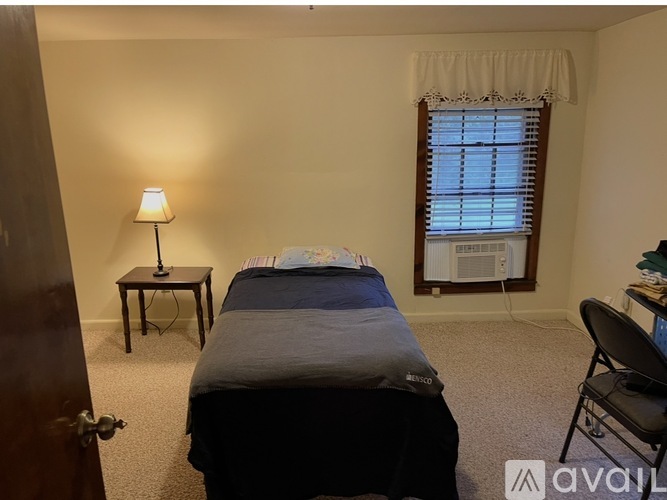 A bedroom with a bed, desk, chair, and window.