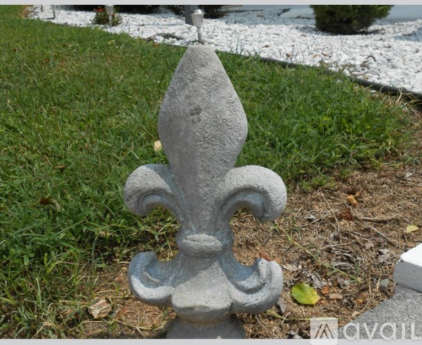 A grey fleur de lis sculpture sits in a grassy area.