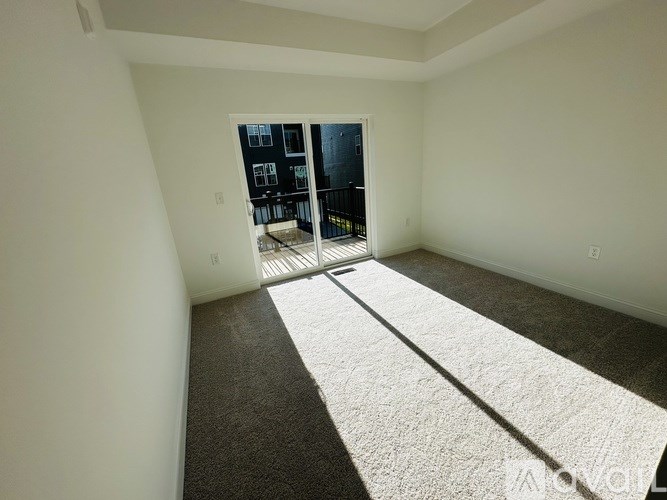 A room with a carpeted floor and a view of a balcony through a glass door.