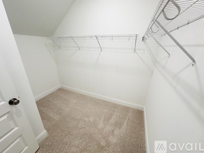 A white door is on the left side of a room with a carpeted floor and a metal rack on the right.