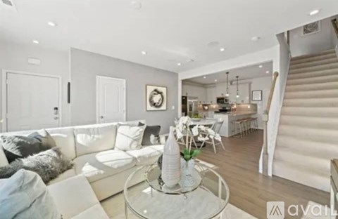 A modern living room with a glass coffee table and a staircase in the background.