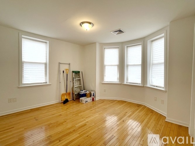 A room with wooden floors and white walls, with a ladder and some boxes on the floor.