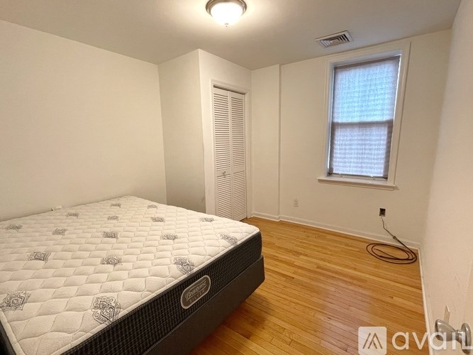 A bedroom with a bed, wooden floor, and a window with blinds.
