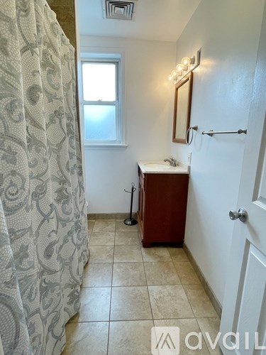 A bathroom with a shower curtain, sink, mirror, and a window.